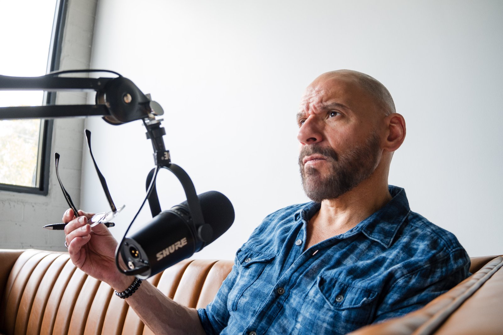 Kevin Rogers at the podcast microphone, holding glasses in contemplation before recording an interview.